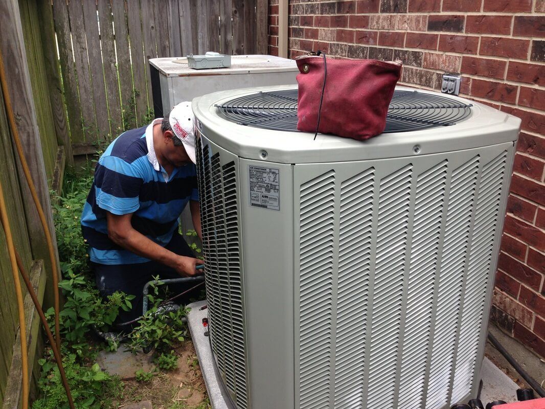 A man is working on an air conditioner outside of a brick building.