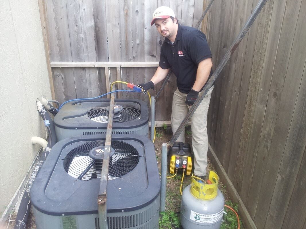 A man is working on two air conditioners in a backyard.