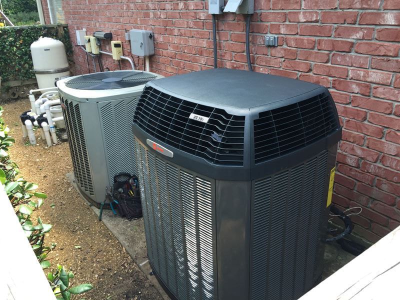 Two air conditioners are sitting on the side of a brick building.