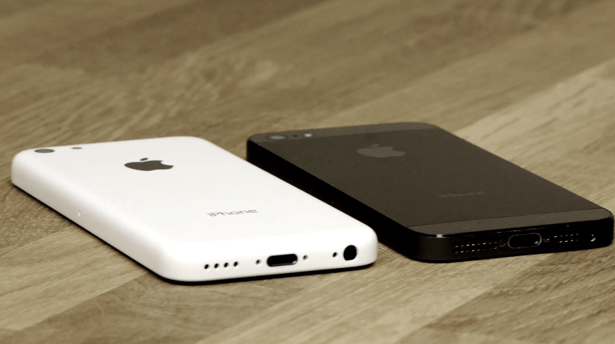White and black smartphones lying face down on a wooden table.