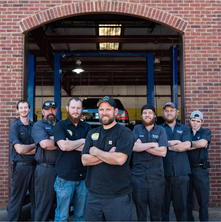 Seven auto mechanics pose in front of a brick building entrance. All have arms crossed, some wear shop uniforms. | Top Quality Car Care