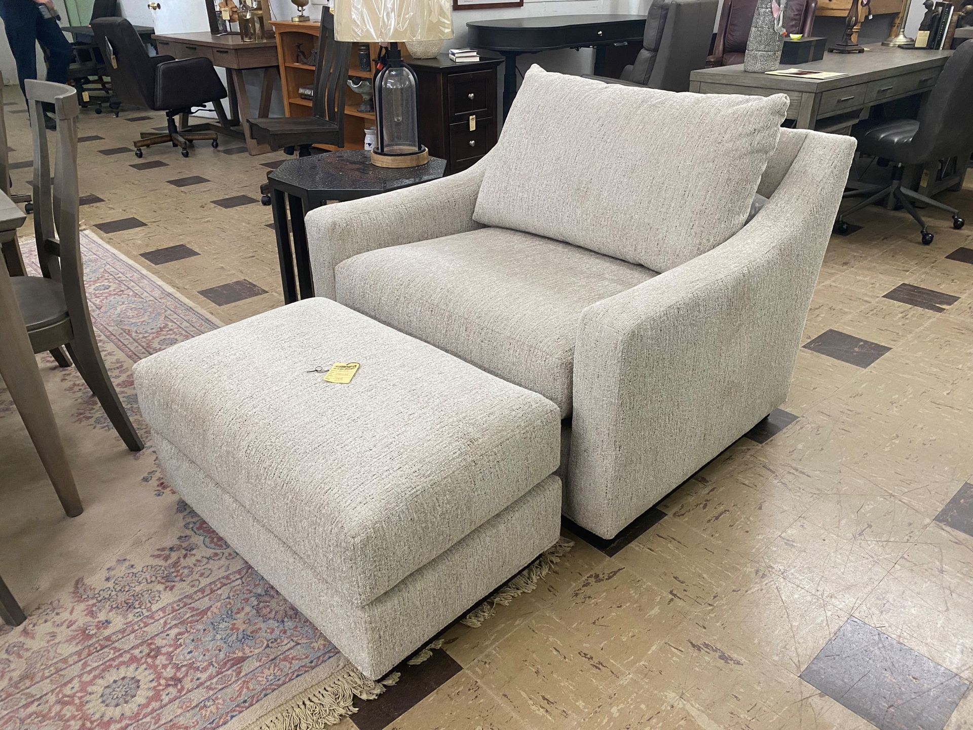 Chair and ottoman set in light textured fabric in a showroom setting.