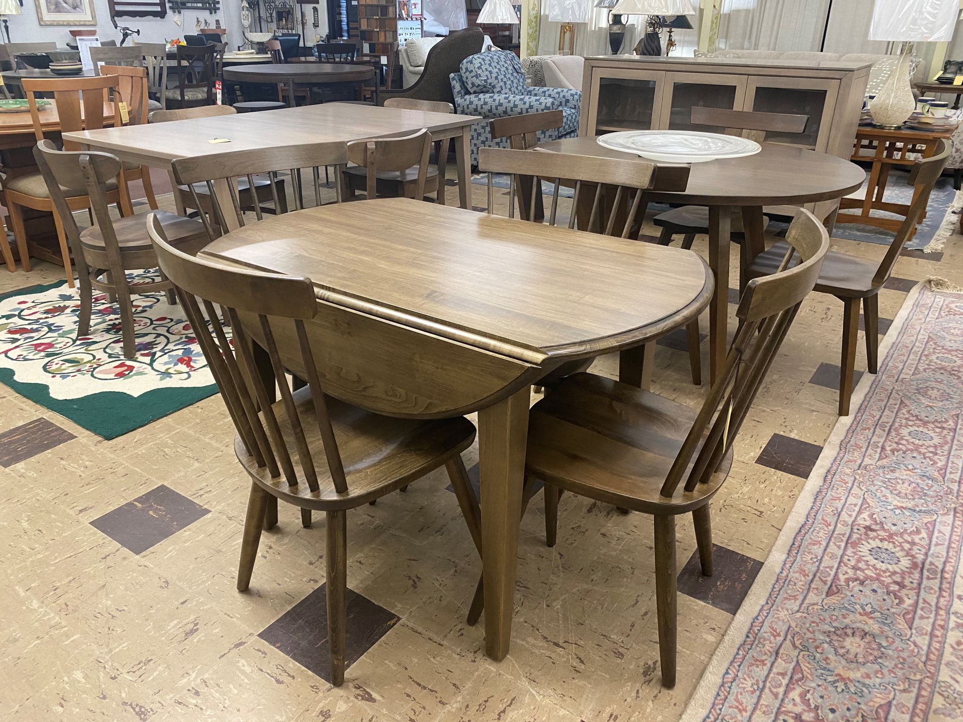Dining sets in a showroom; a round table with 4 chairs, other tables & furniture in the background.