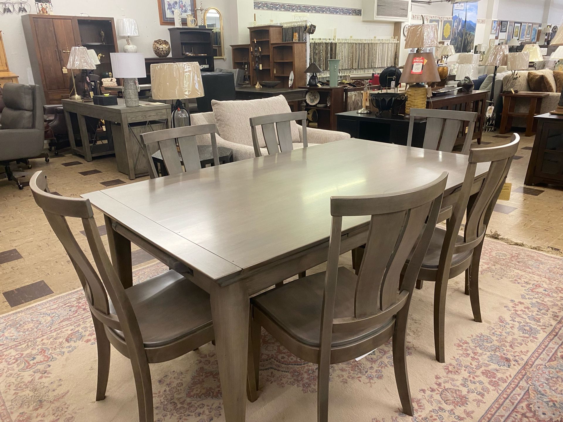 A dining room set with a rectangular gray table and six matching chairs in a furniture store.
