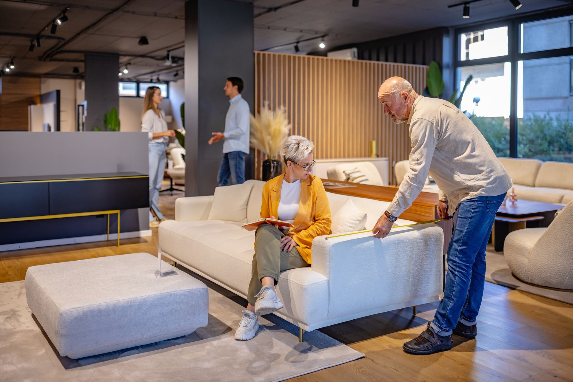 A mature man is focused on measuring a modern couch.