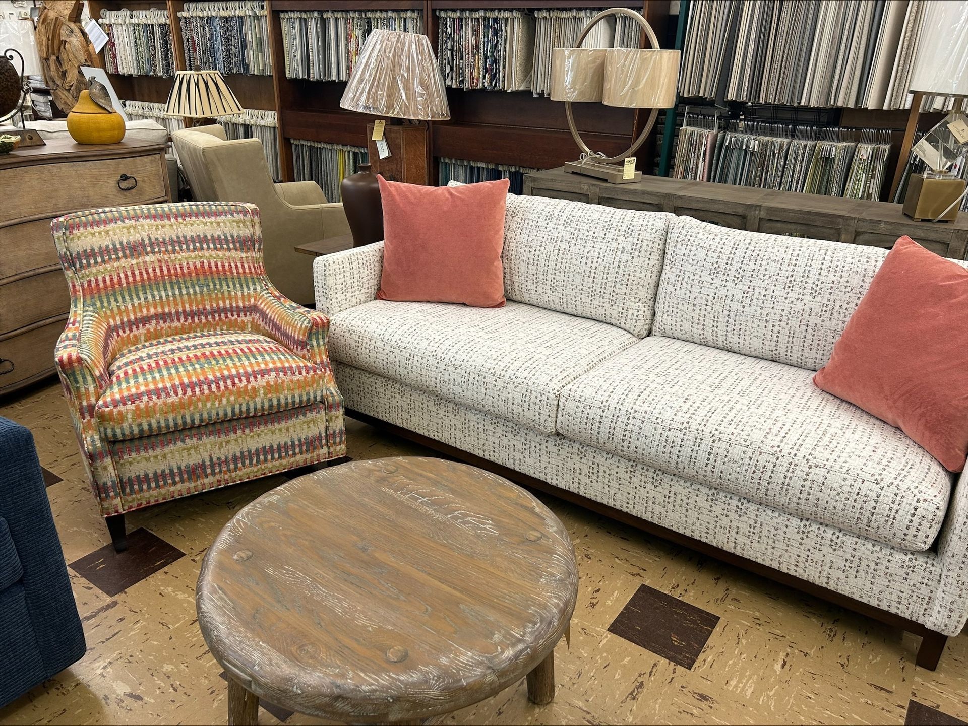 Living room furniture display. White patterned sofa with coral pillows, patterned armchair, round coffee table.