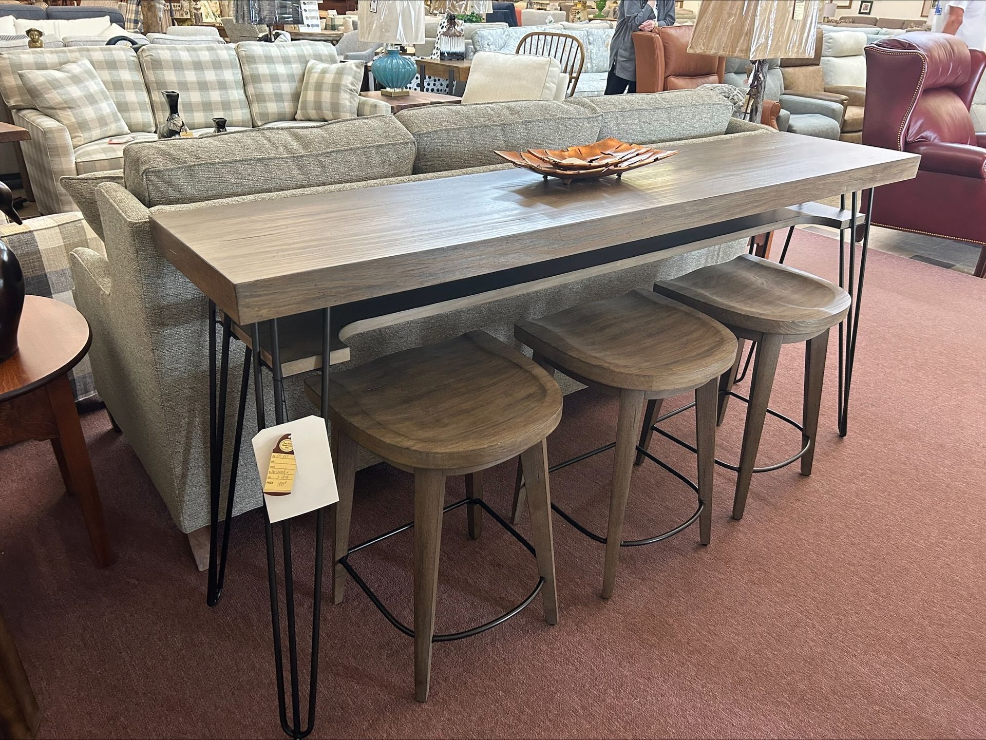 Sofa with attached bar table and three stools, brown tones, in a furniture store.