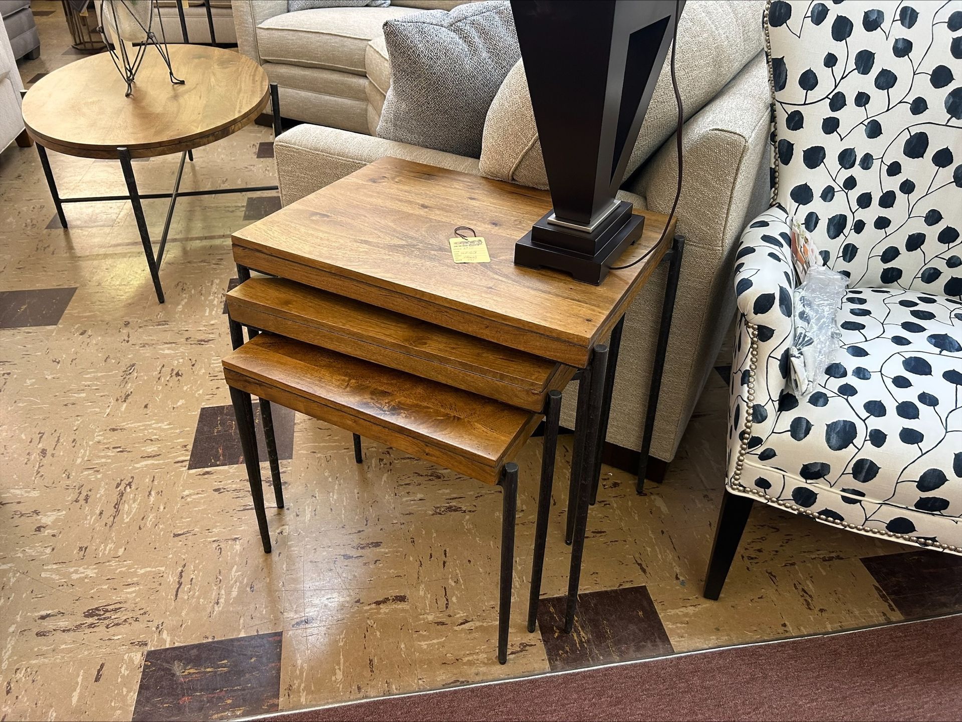 Three nesting tables, topped with wood, sit beside a patterned armchair and neutral sofa.