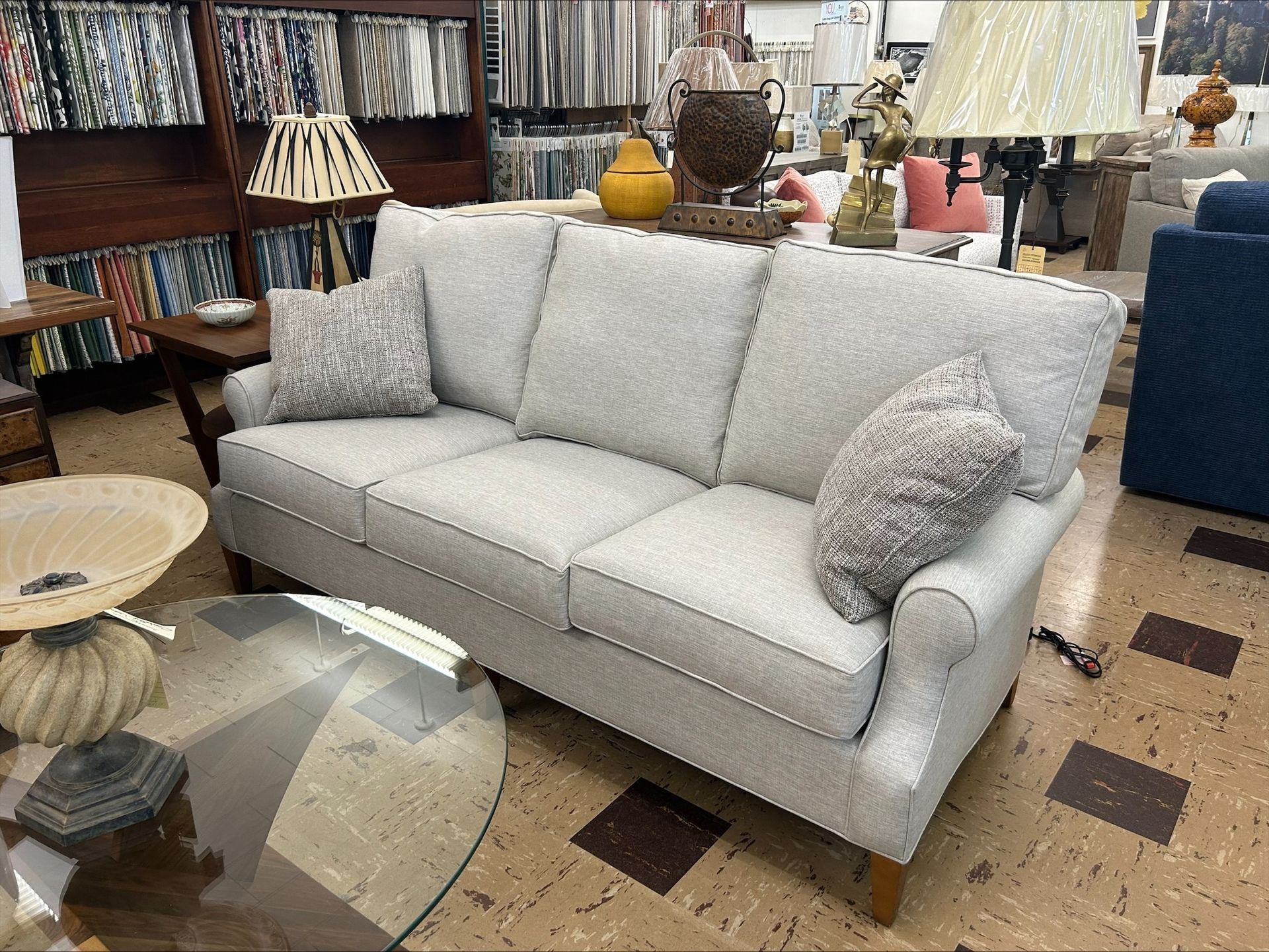 A neutral-toned sofa with two patterned pillows in a showroom setting.