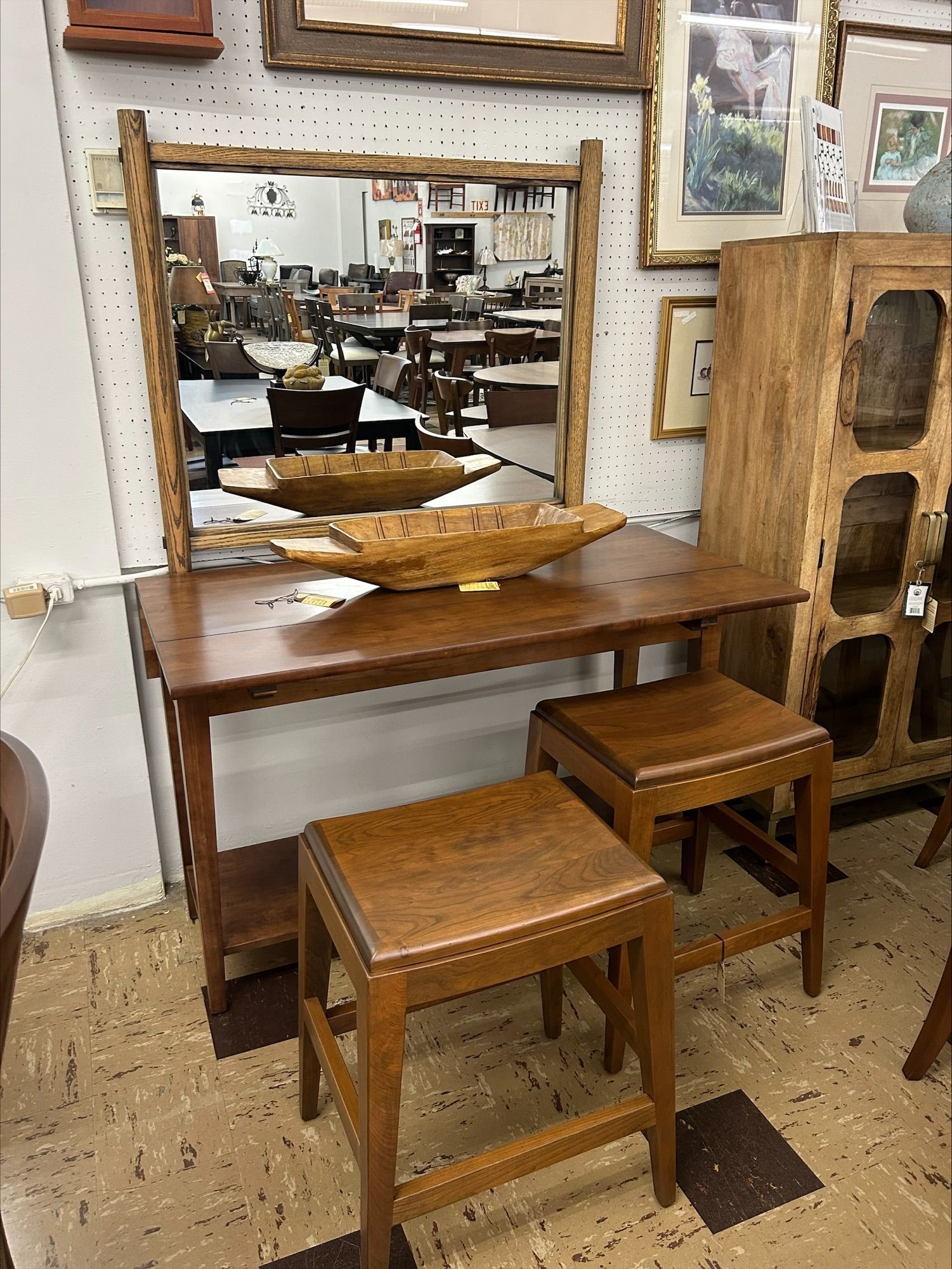 Vanity table with mirror, two stools, and decorative wooden bowls, in a shop.