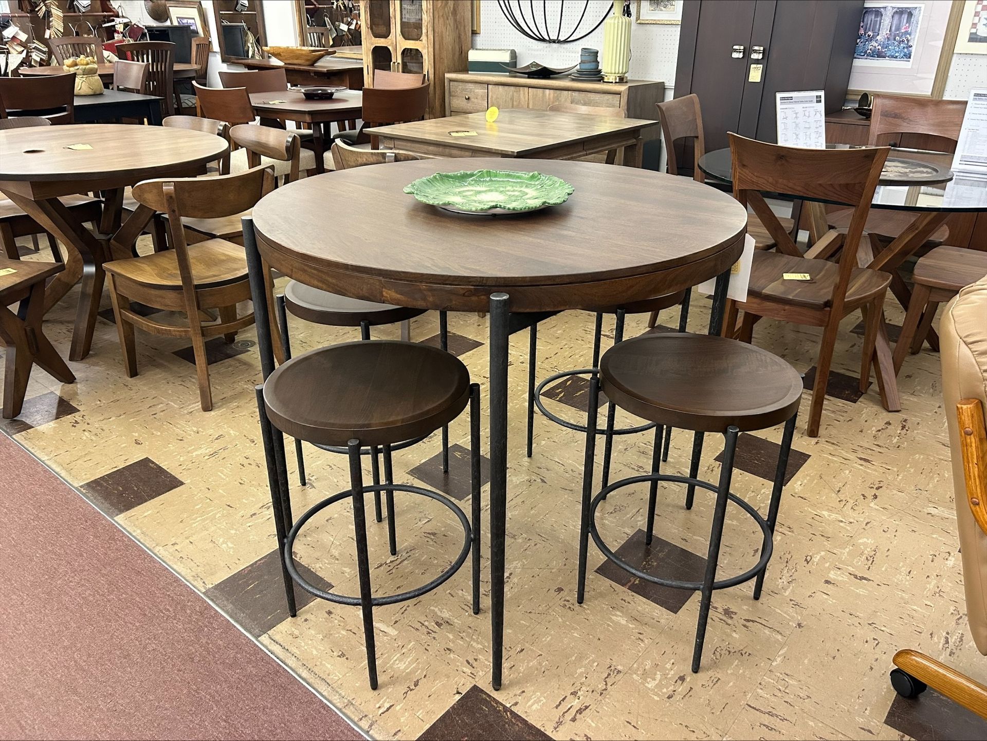 Round table with three stools in a shop. Dark wood, metal legs, patterned floor.