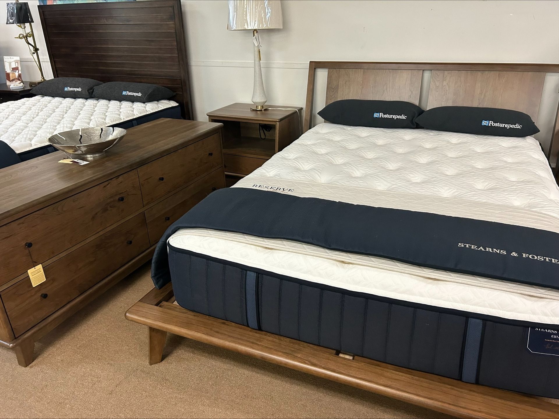 Bedroom furniture display: beds, dresser, nightstand, and lamp in a showroom.