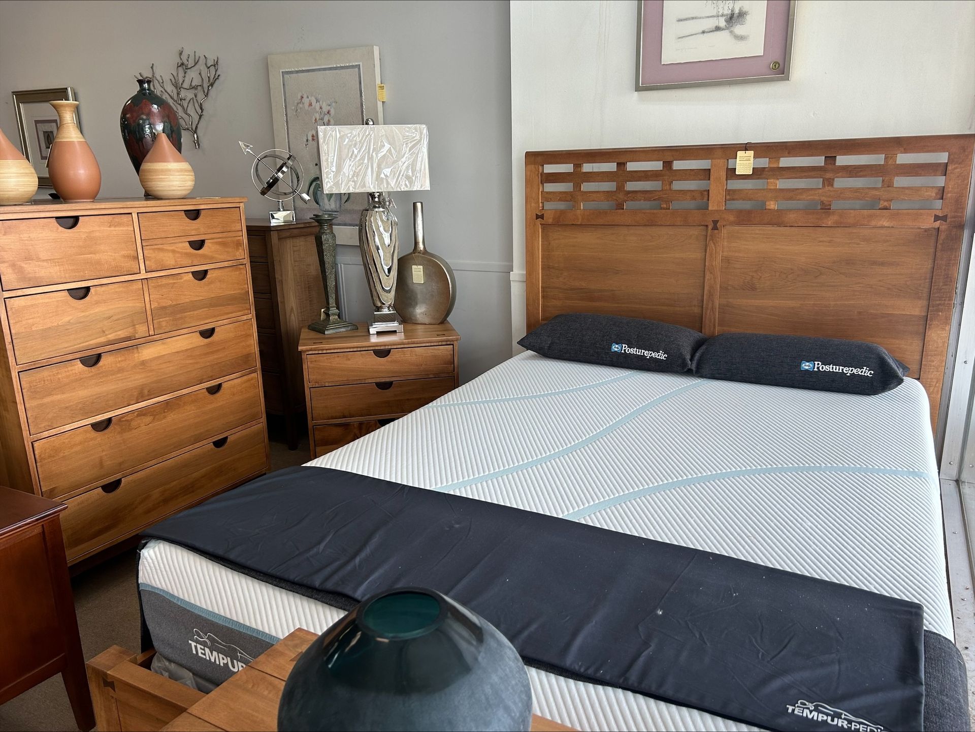 Bedroom furniture set: wooden bed frame, chest of drawers, nightstand, lamp, and decorative vases.