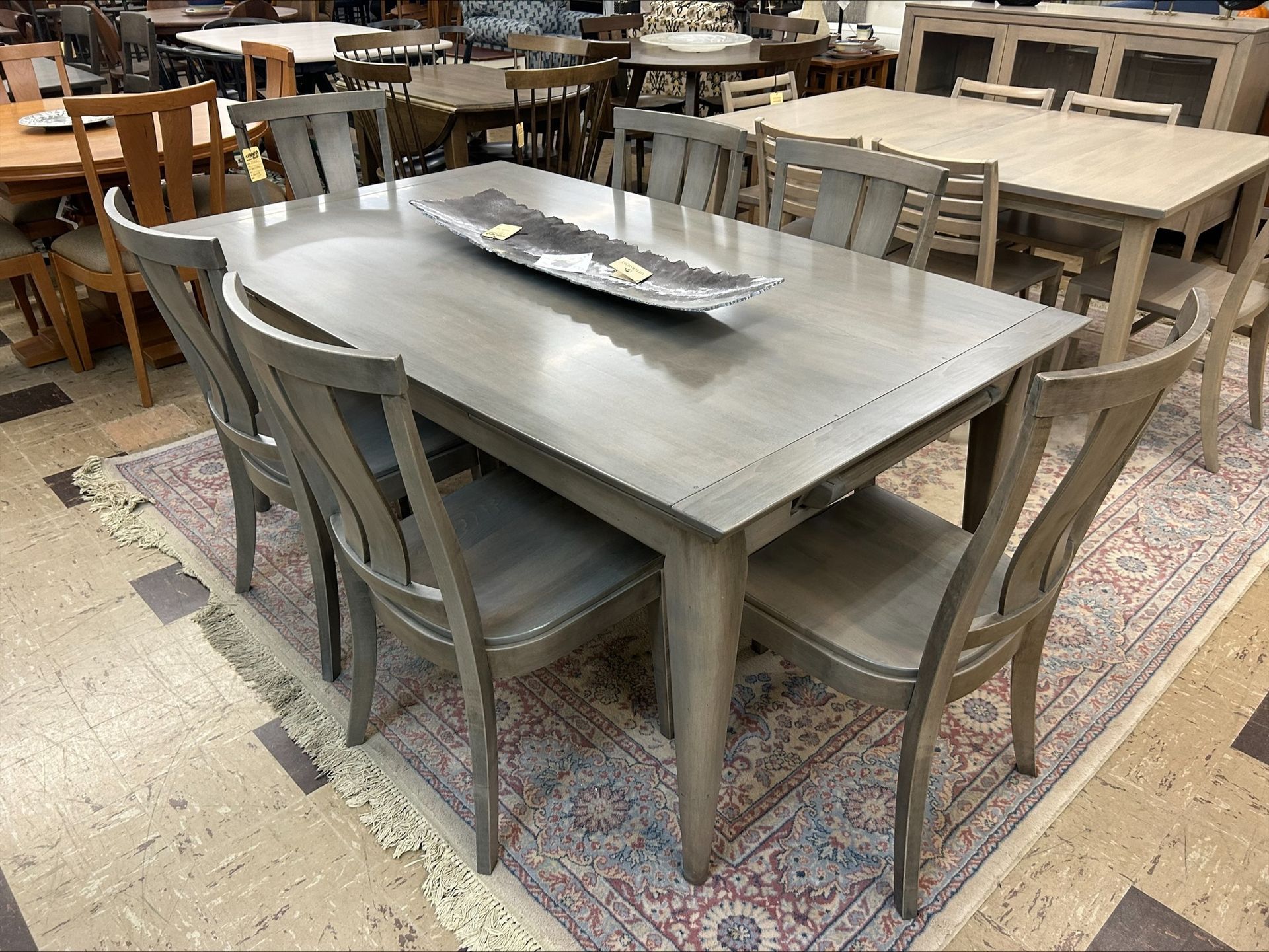 Gray dining table with six matching chairs on a patterned rug. Other furniture is visible in the background.