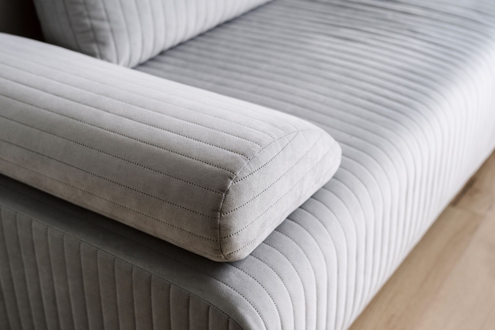 Close up of modern grey upholstered sofa with textured fabric and armrest detail.