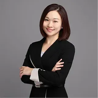 A woman in a black suit is standing with her arms crossed and smiling.