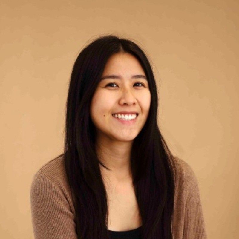A woman with long red hair is standing in front of a tree and looking at the camera.