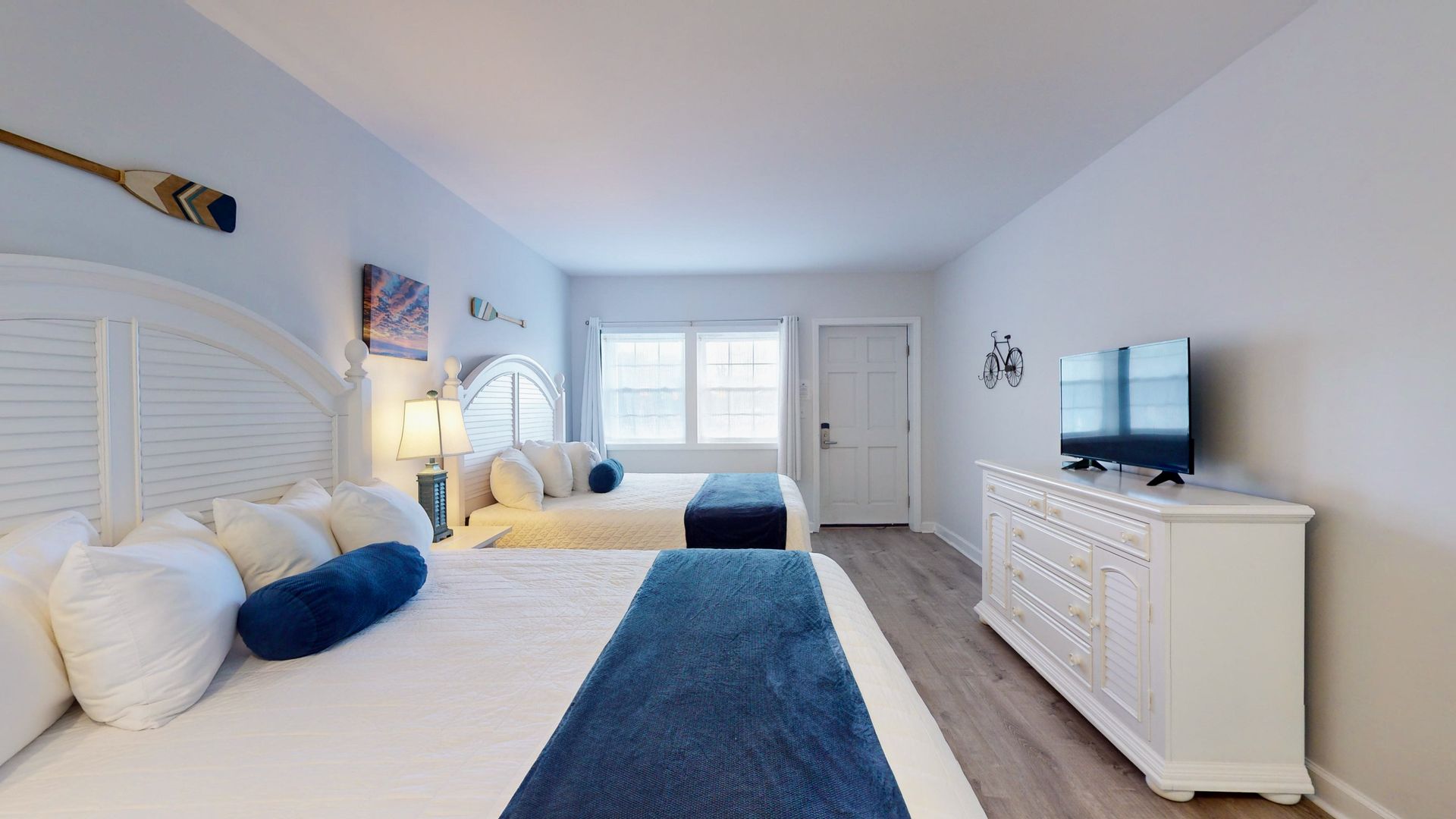 A hotel room with two beds , a dresser and a flat screen tv.
