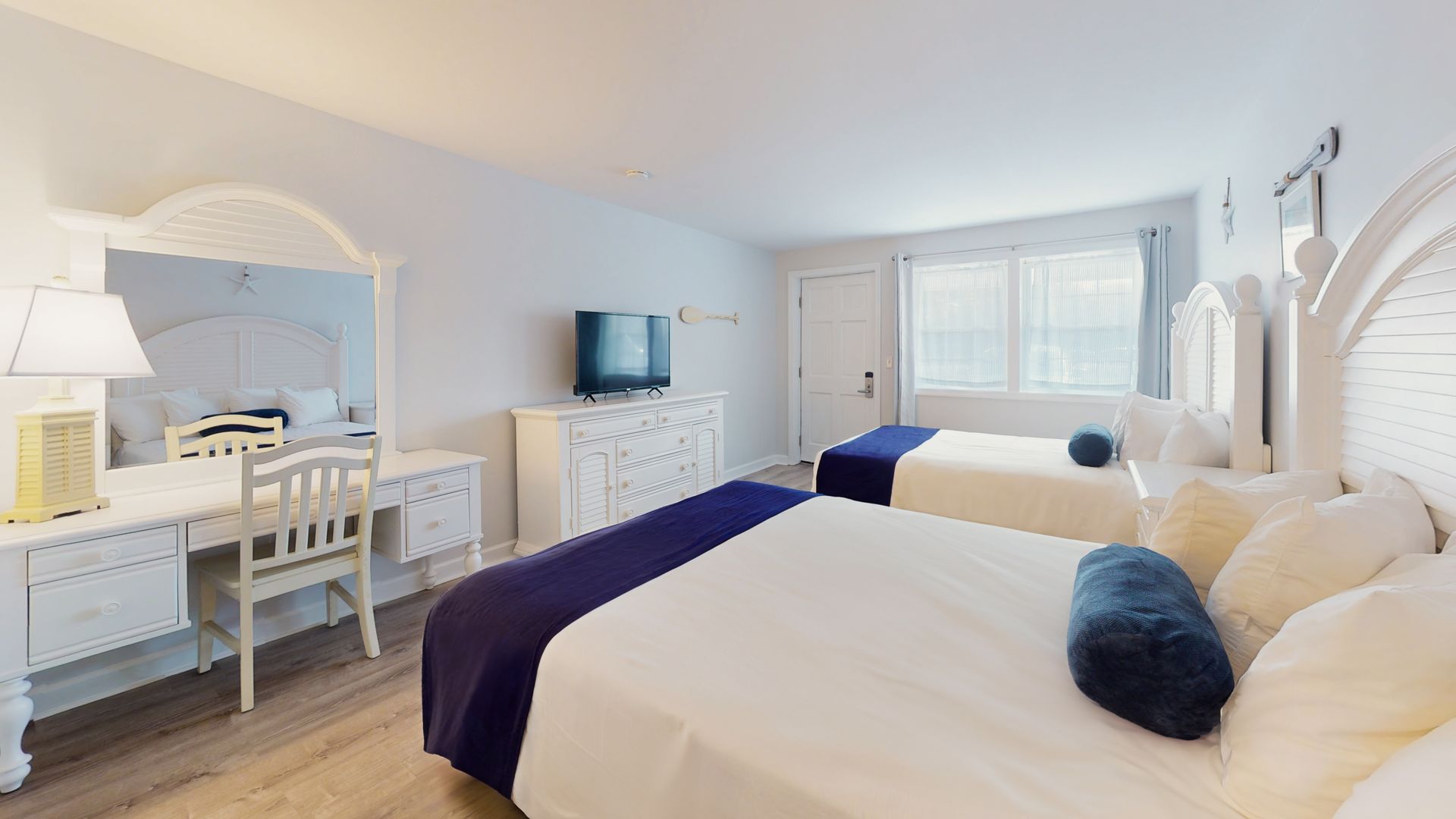 A hotel room with two beds , a desk , a television and a mirror.