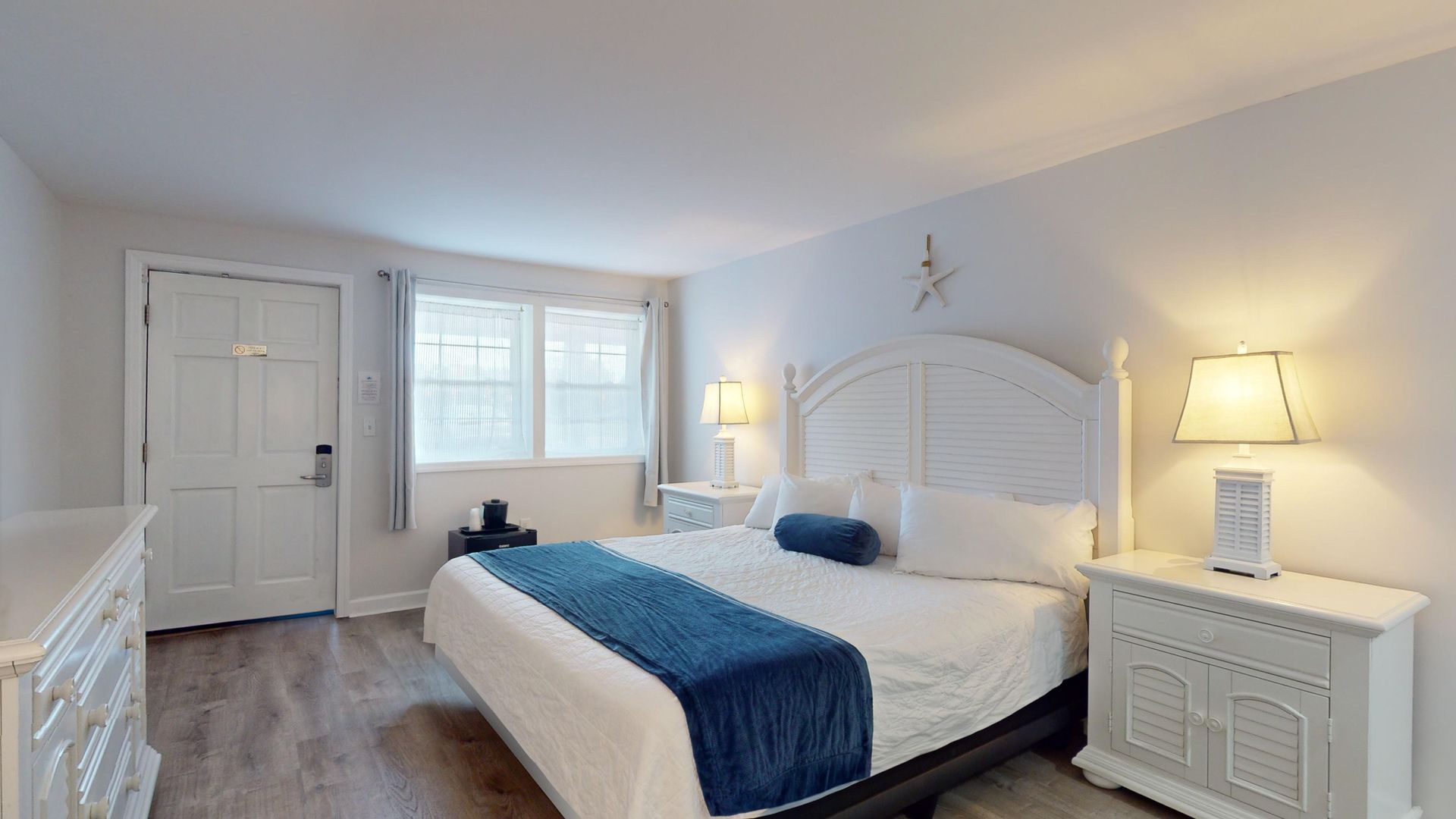 A bedroom with a king size bed , dresser , nightstand , and two lamps.