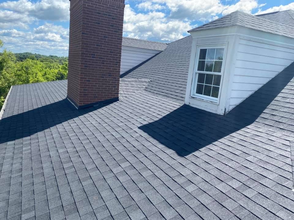 Gray shingled roof with a brick chimney, white dormer, and a cloudy blue sky.