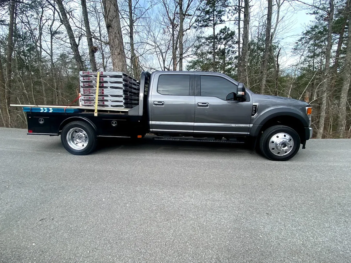 Gray flatbed truck carrying a load of gray pavers on an asphalt road.
