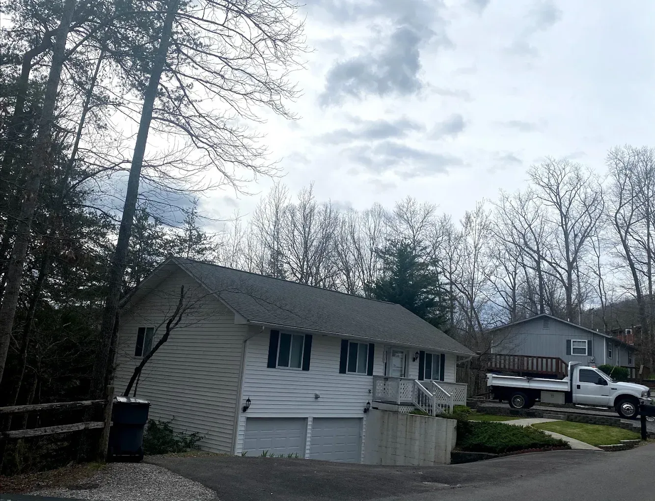 White house with garage, surrounded by trees, gray sky. A pickup truck is parked nearby.