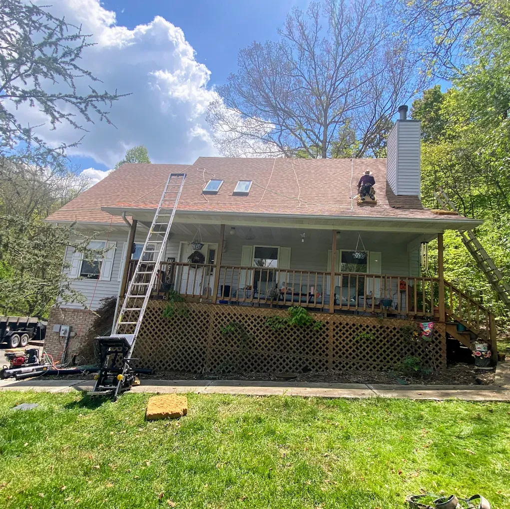 Roofers working on a house; ladder propped against the roof, sunny day, green grass.