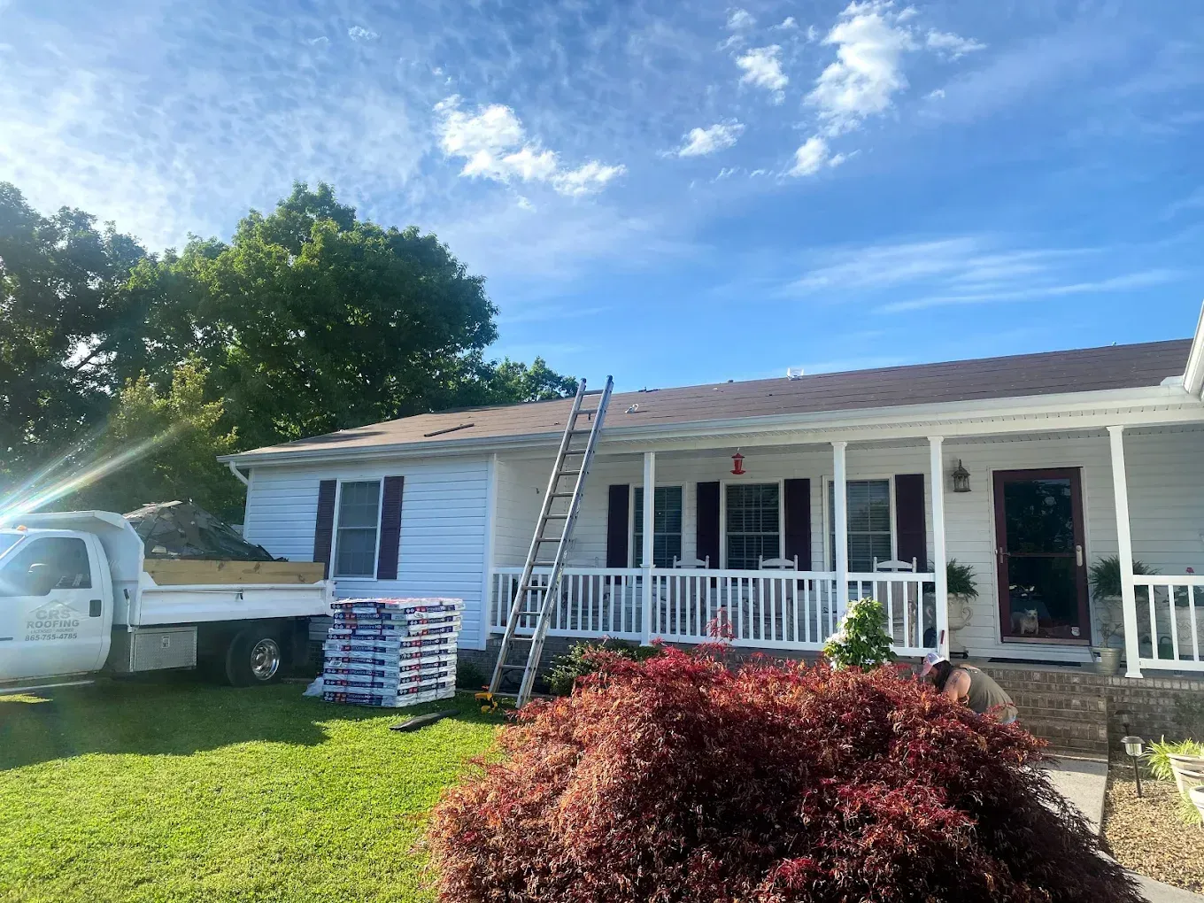 White house with a roof being worked on, ladder, truck, and building materials visible.