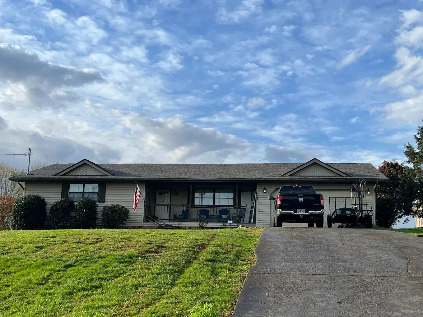 A tan ranch house with a dark truck parked in the driveway under a cloudy sky.