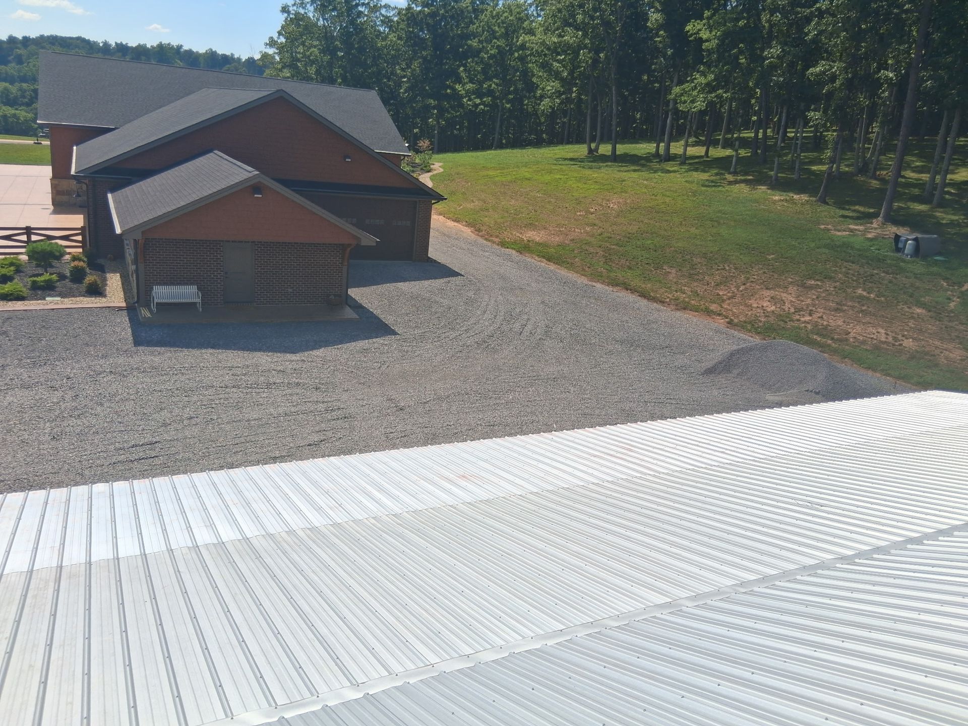A view from above showing a white metal roof overlooking a gravel driveway and a brown house with a garage.