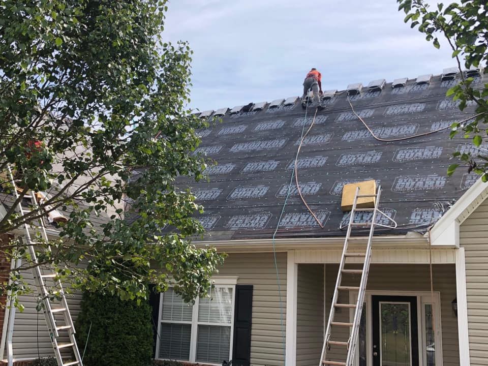 Person on a roof, removing shingles; ladders alongside a home.