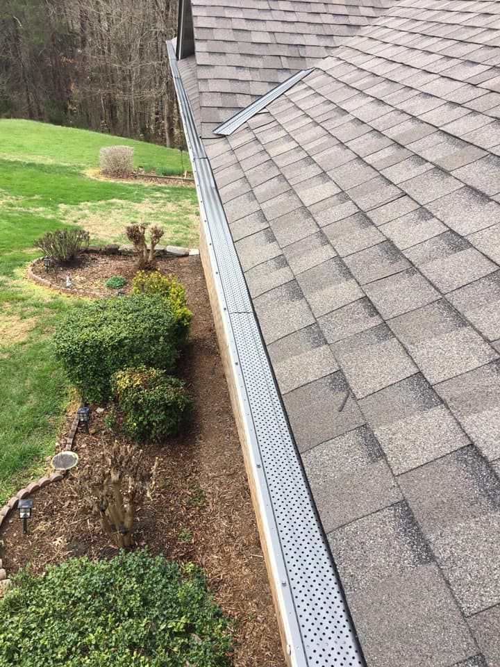 A roof with gray shingles and a gutter guard. The gutter runs alongside the roof near a landscaped garden.