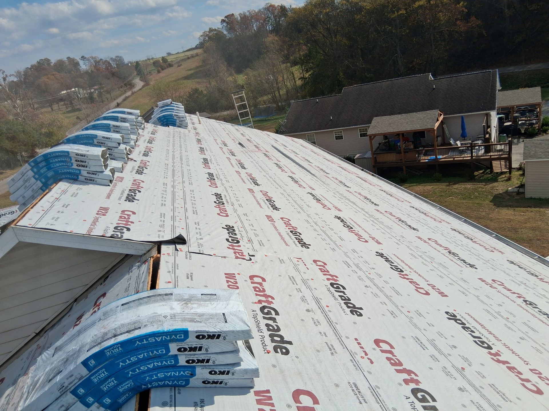 A partially shingled residential roof under construction, featuring white underlayment and stacks of roofing material.