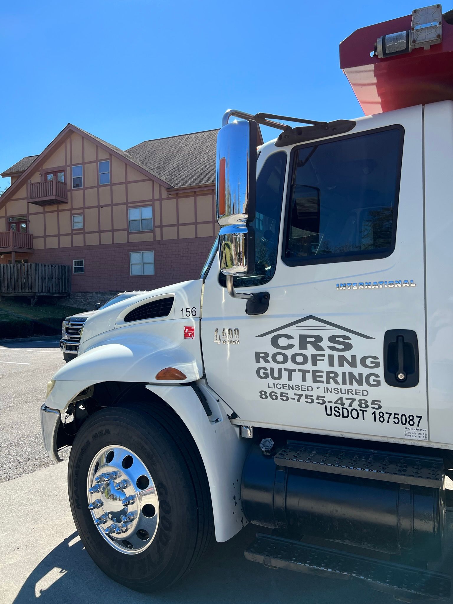 A side view of a white dump truck parked in front of a multi-story building, labeled with 