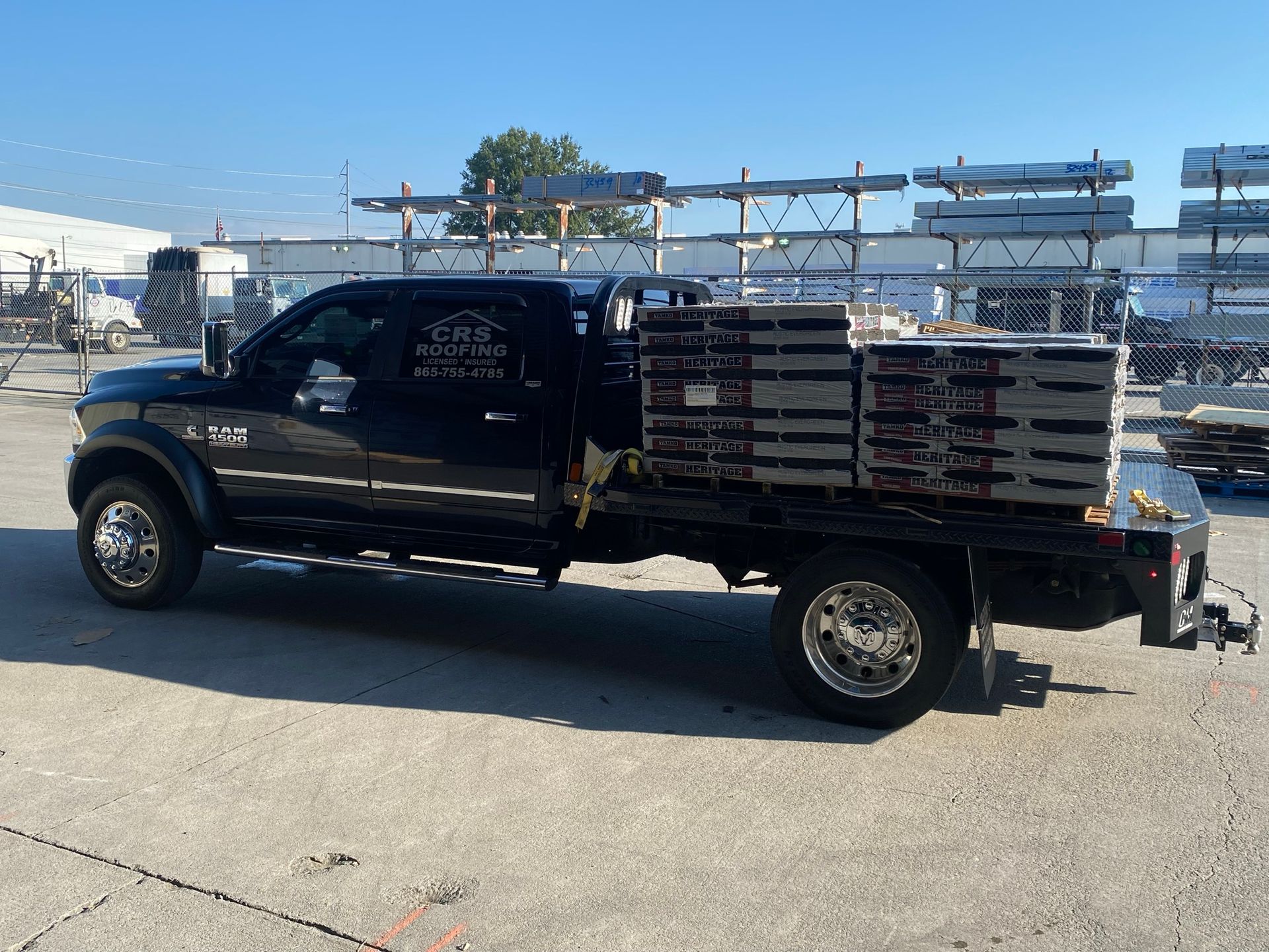 A black flatbed pickup truck loaded with stacked construction materials sits in an outdoor industrial lot.
