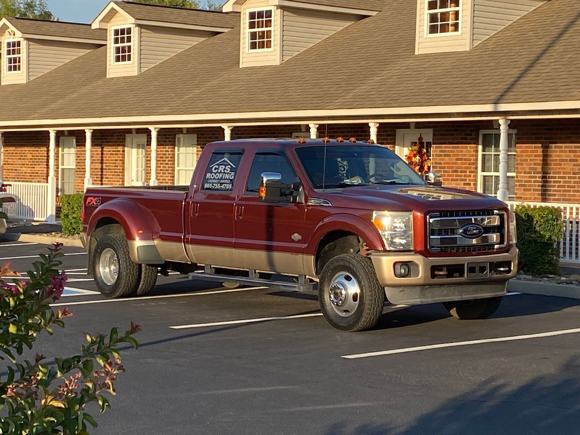 A maroon and tan Ford dually pickup truck parked in a brick building parking lot.