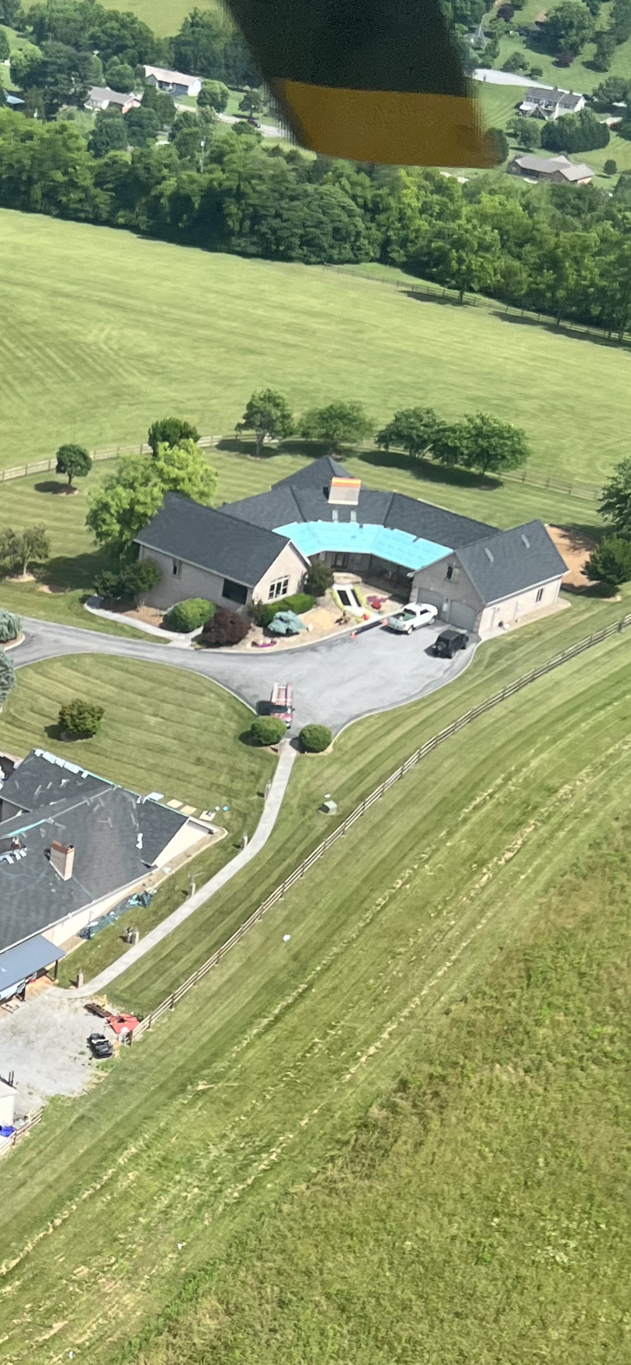 Aerial view of a sprawling house with a large, curved swimming pool in a rural, grassy landscape.