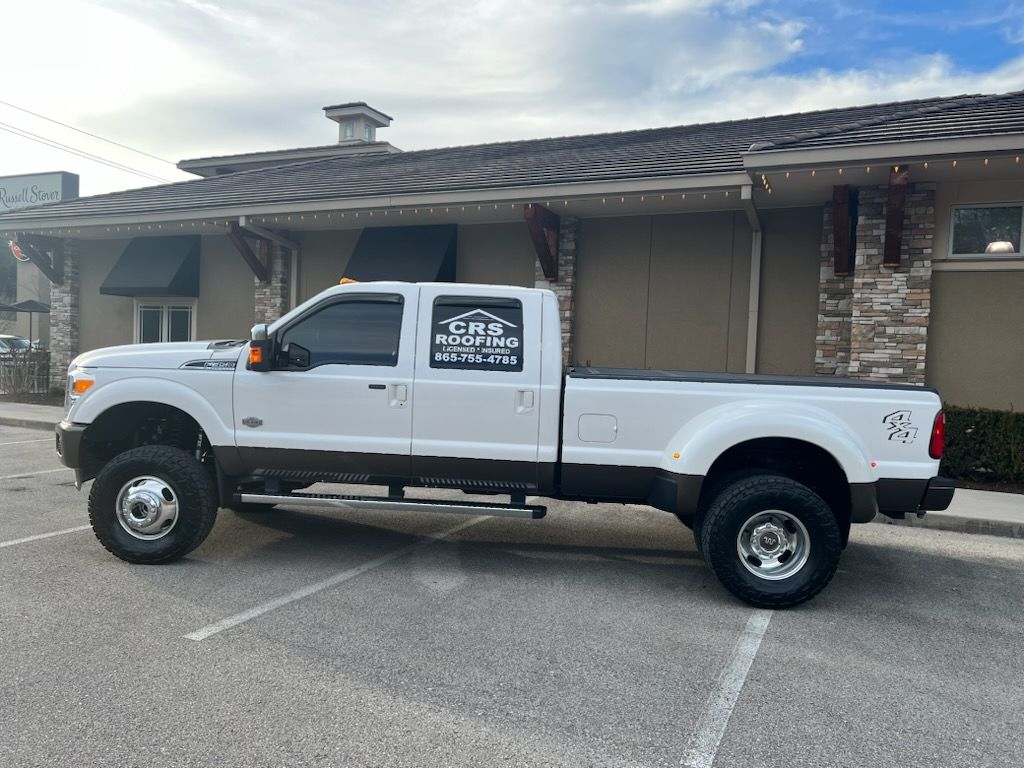 A white Ford F-350 dually pickup truck parked in a commercial lot, featuring brown lower trim and a For Sale sign.