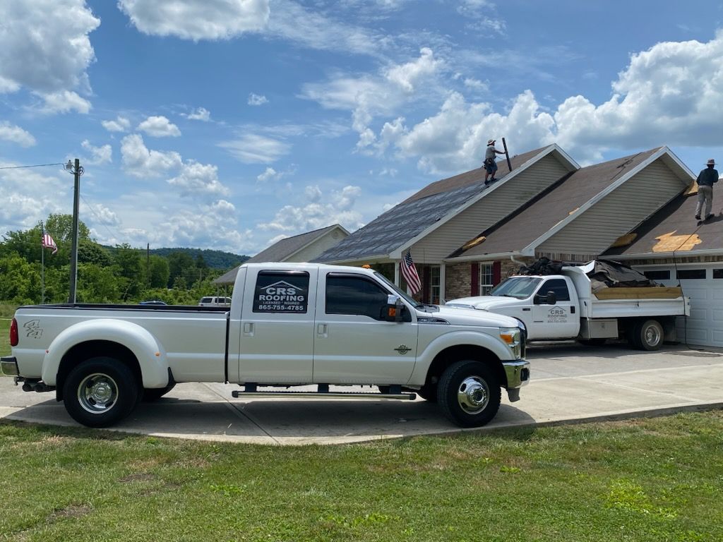 Workers on a residential roof installing solar panels with two white work trucks parked in the driveway.