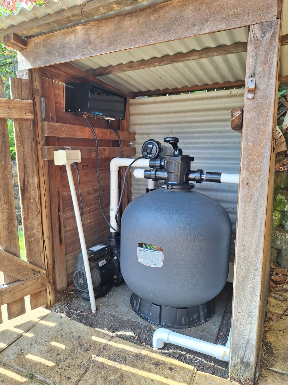 A swimming pool filter is sitting inside of a wooden shed.