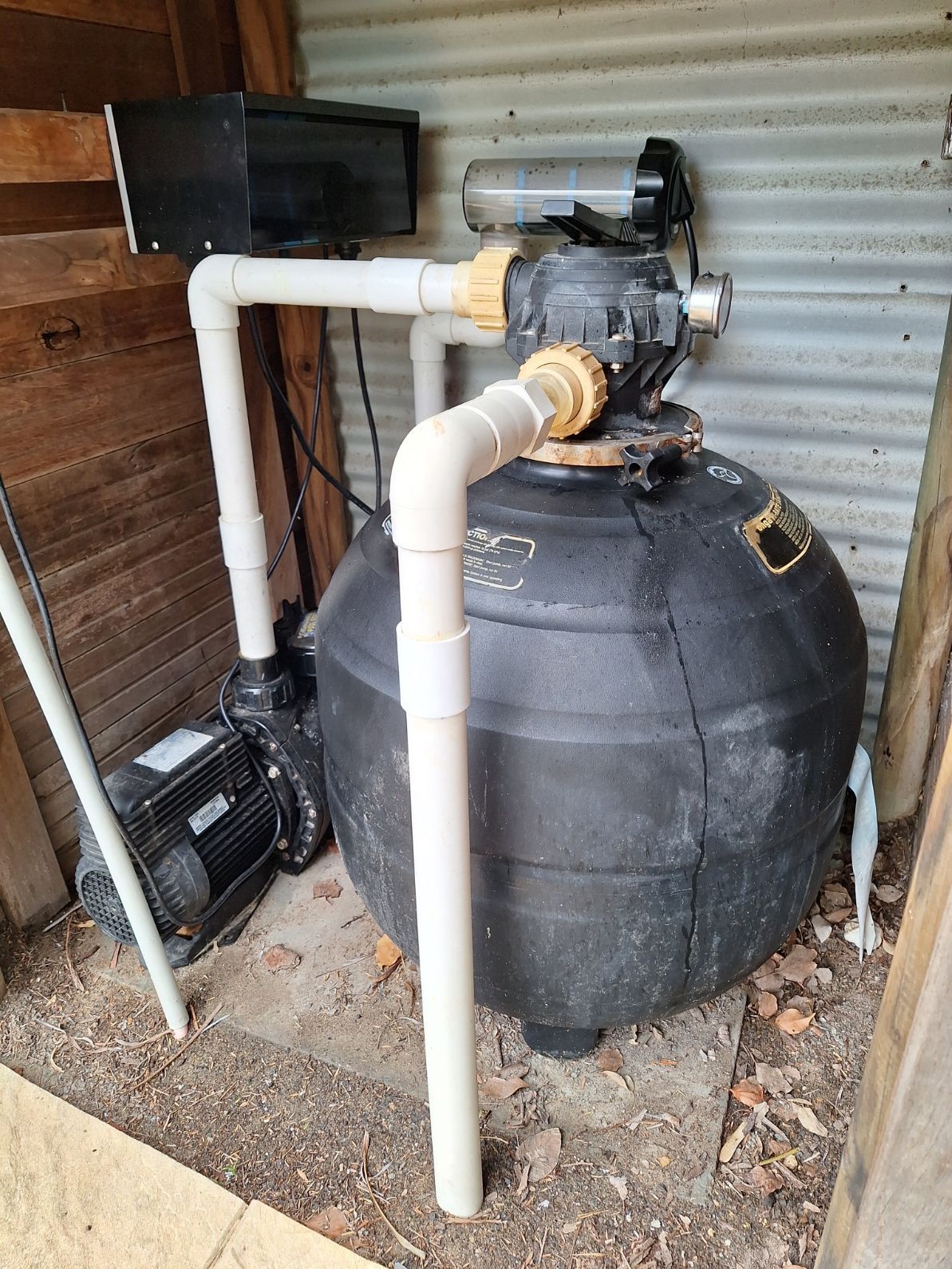 A pool filter is sitting in a shed next to a pump.