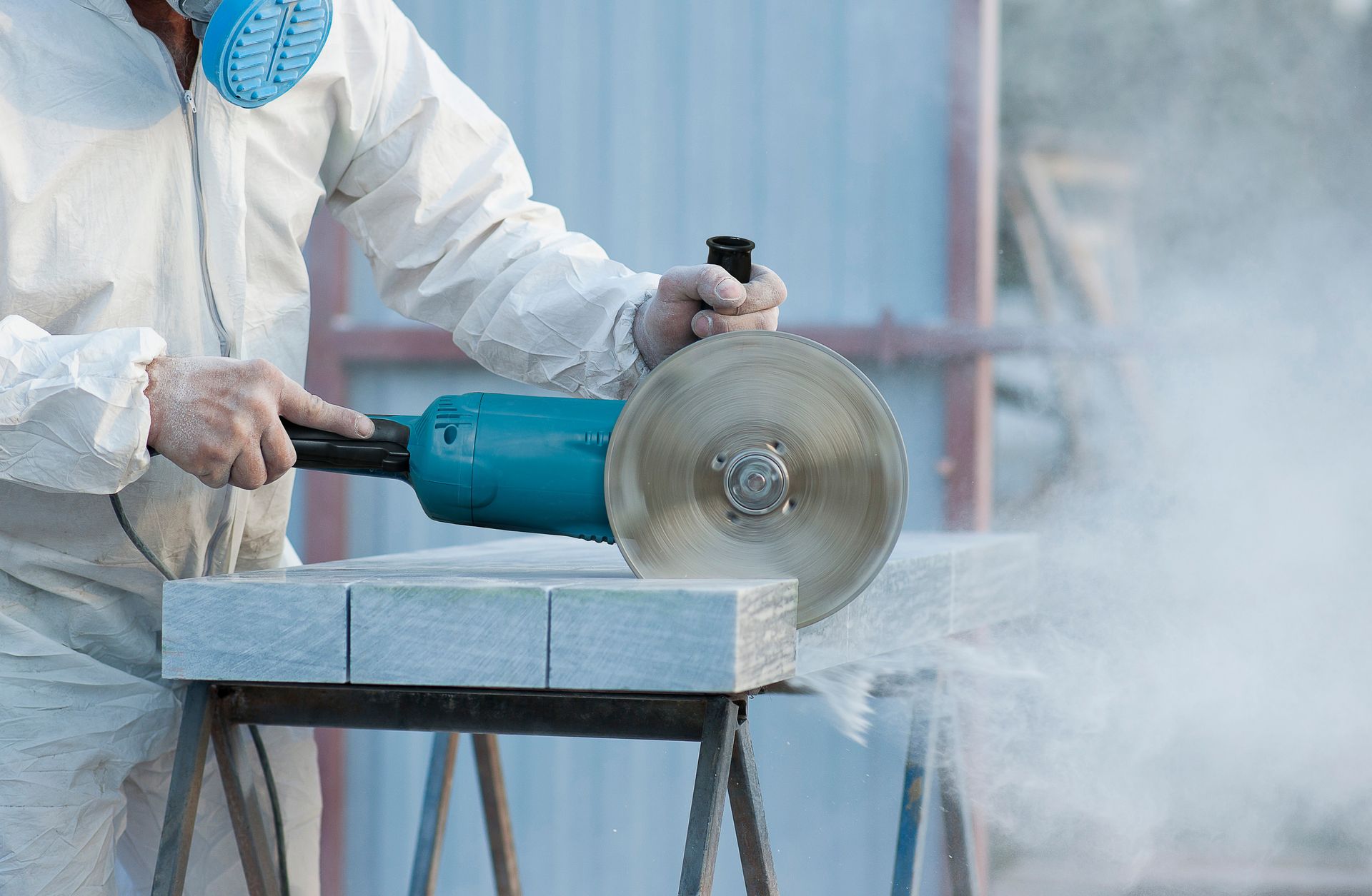 Person wearing protective gear uses a power grinder to cut stone, creating dust.