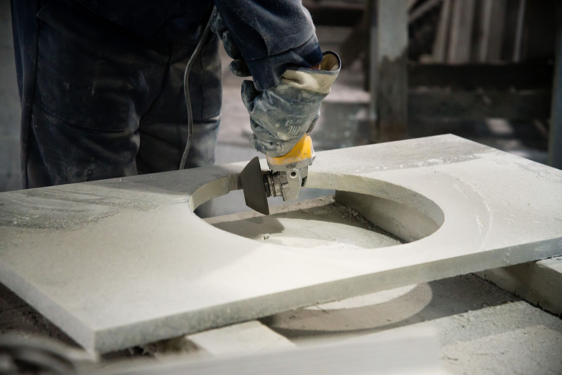 A person uses a power tool to cut a circular hole in a stone countertop.