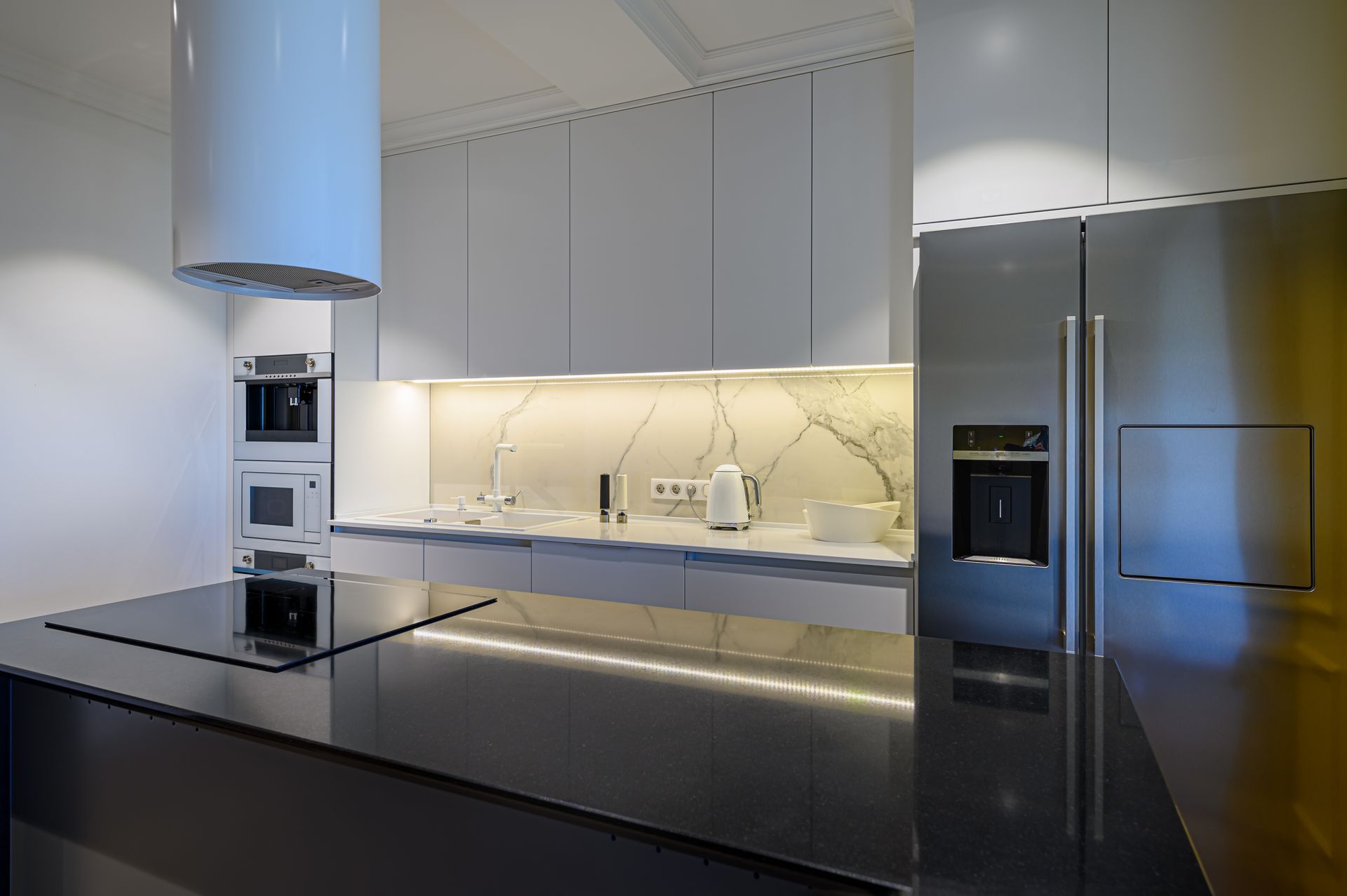 Modern kitchen with white cabinetry, marble backsplash, stainless steel refrigerator, and black island.