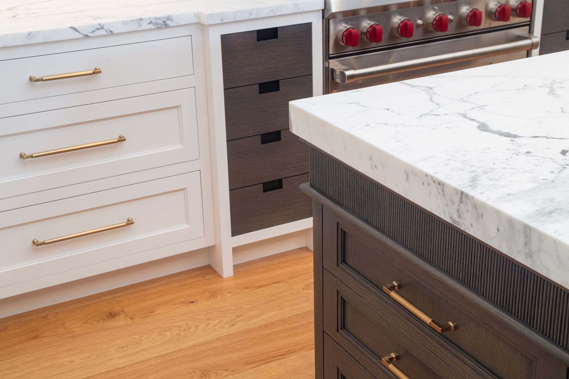 Kitchen with white cabinets, dark island, gold hardware, and marble countertops.