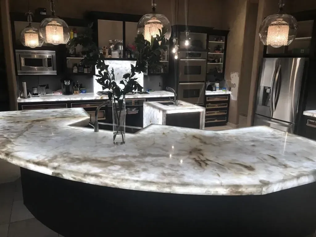 Modern kitchen with a large, lit marble countertop island and pendant lights.