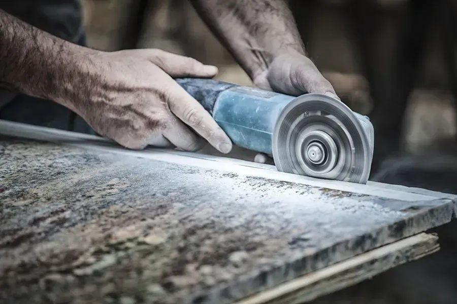 Person using a power grinder on a stone surface, creating dust.