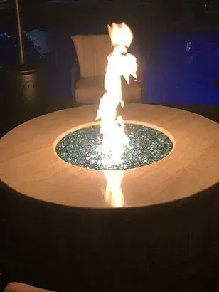 Fire pit with tall flames and blue glass stones, set on a beige table; lit at night.