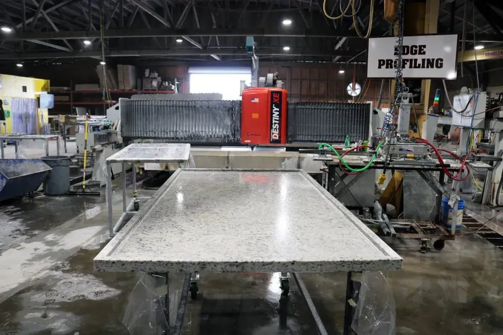 A large granite countertop being worked on by a robotic machine in a factory setting.